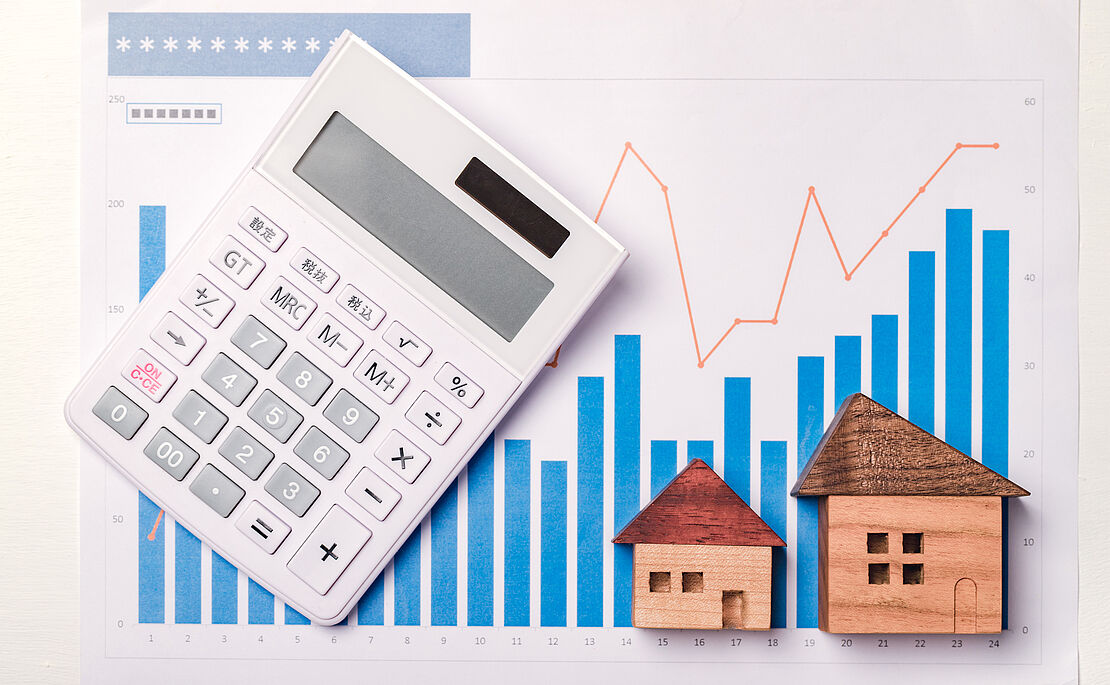 Stabdiagramm Entwicklung der Zinsen bei Immobilienkrediten mit zwei Holzhäuschen und einem Taschenrechner