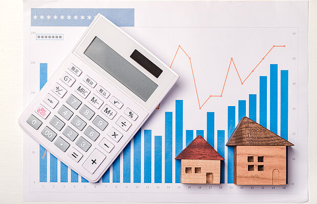 Stabdiagramm Entwicklung der Zinsen bei Immobilienkrediten mit zwei Holzhäuschen und einem Taschenrechner