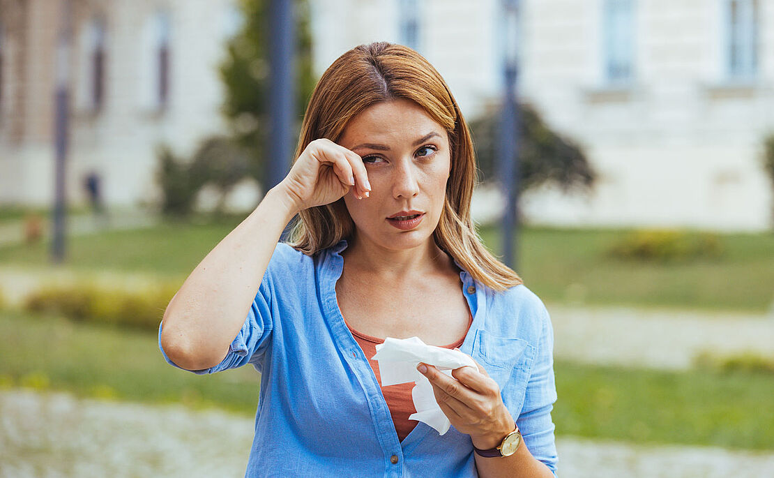 Frau mit Taschentuch in der Hand, mit der anderen Hand wischt sie beim Auge