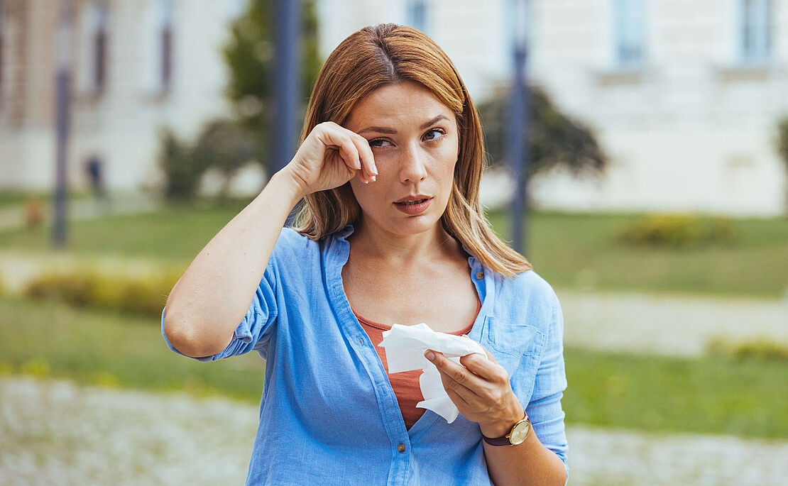 Frau mit Taschentuch in der Hand, mit der anderen Hand wischt sie beim Auge
