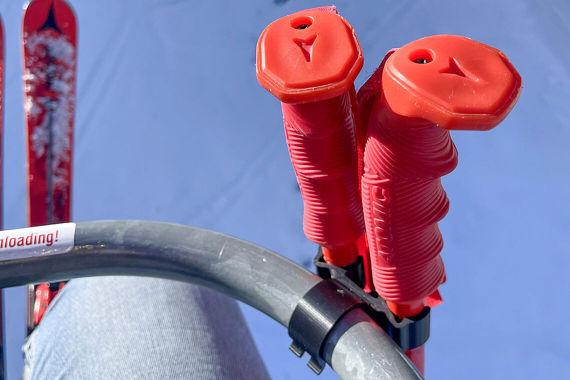 Ausschnitt eines Liftbügels, daran befestigt Skistöcke