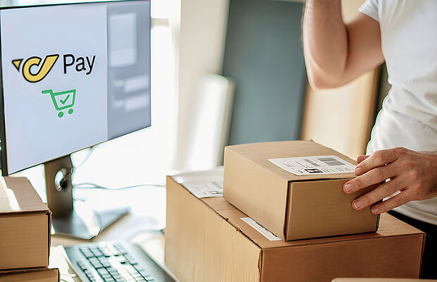 Zwei Pakete vor einem Bildschirm mit dem Post Pay Logo