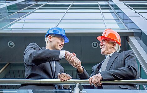 Zwei Männer auf der Baustelle mit Bauhelm am Kopf, die sich die Hände schütteln