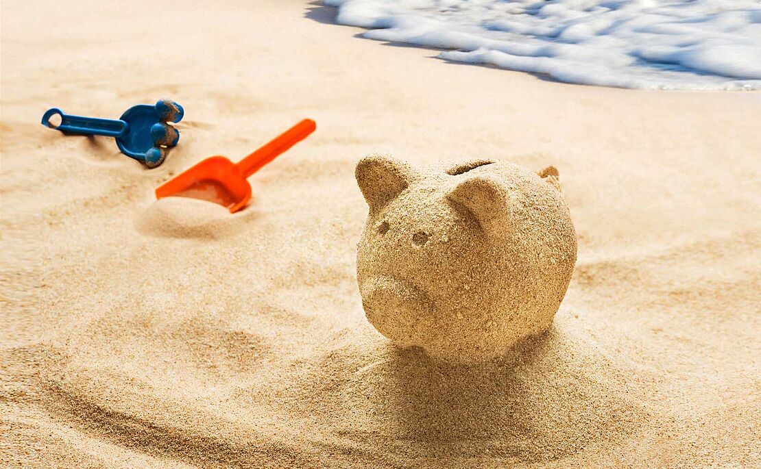 Strand mit Meer und Sandspielzeug, und ein Sparschwein aus Sand