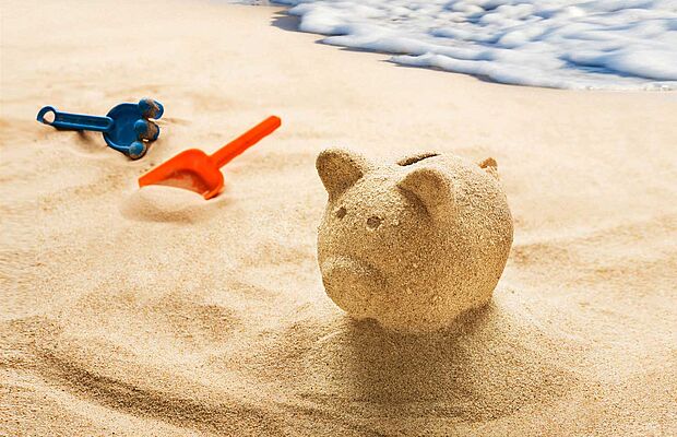 Strand mit Meer und Sandspielzeug, und ein Sparschwein aus Sand