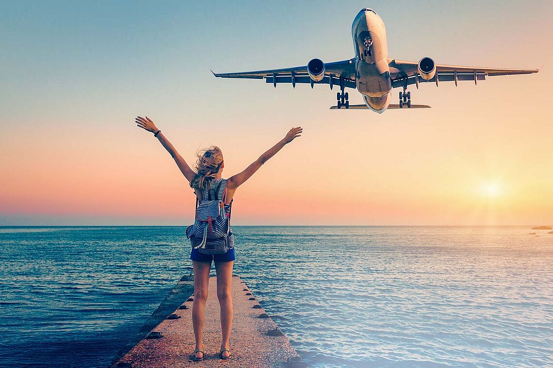 Foto einer Frau mit Rucksack am Meer, in der Luft fliegt ein Flugzeug