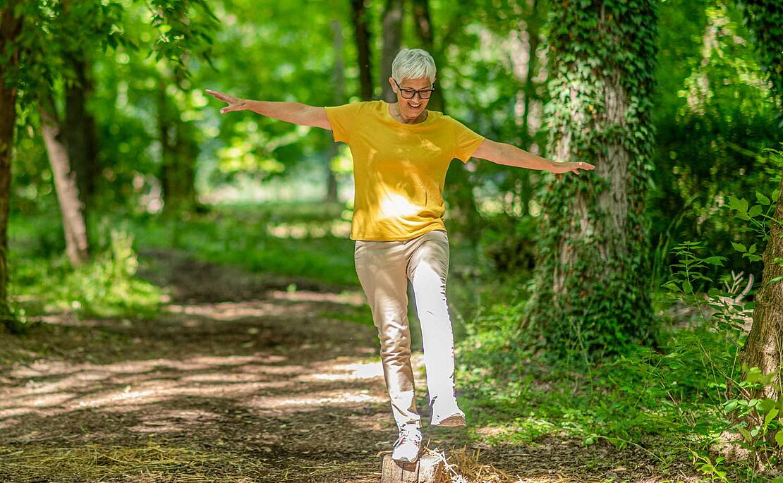 Frau, die einen Einbeinstand im Park auf einem Stein macht