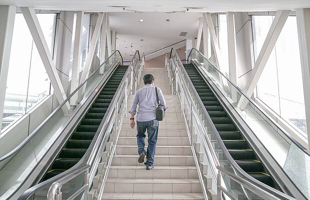 Mann steigt Treppe hinaus, links und rechts davon sind Rolltreppen