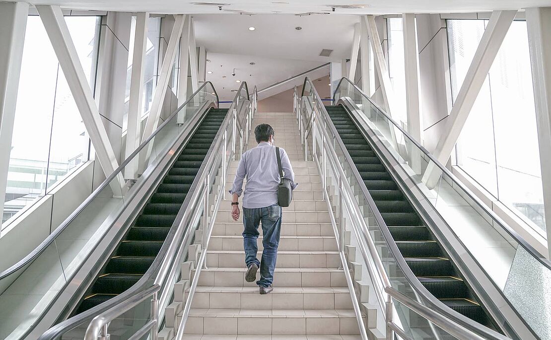 Mann steigt Treppe hinaus, links und rechts davon sind Rolltreppen