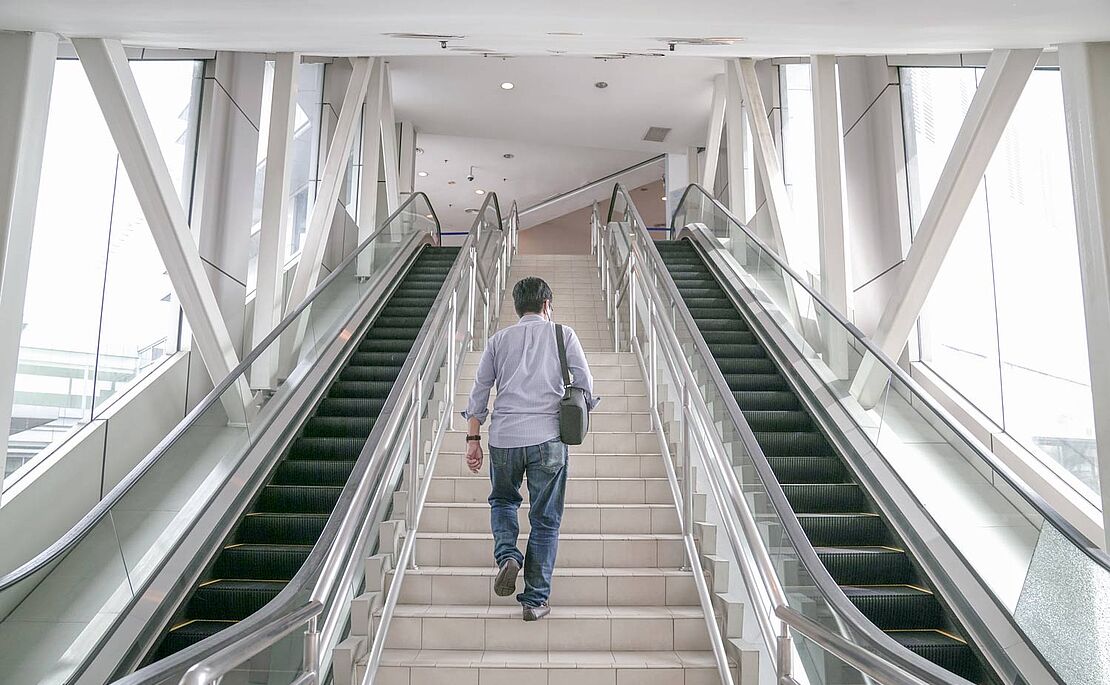 Mann steigt Treppe hinaus, links und rechts davon sind Rolltreppen