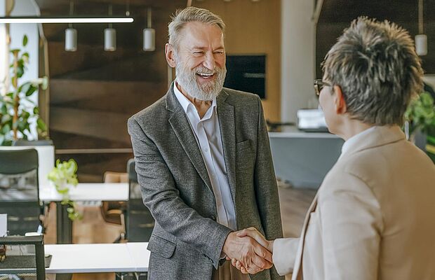 Ein lachender vollbärtiger Mann beim Handschlag mit einer kurzhaarigen Frau