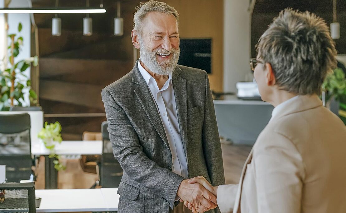 Ein lachender vollbärtiger Mann beim Handschlag mit einer kurzhaarigen Frau