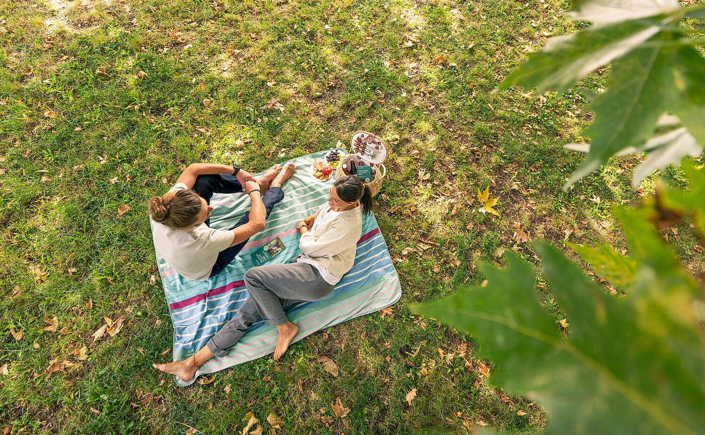 Mann und Frau sitzen auf einer Decke auf einer Wiese und machen ein Picknick