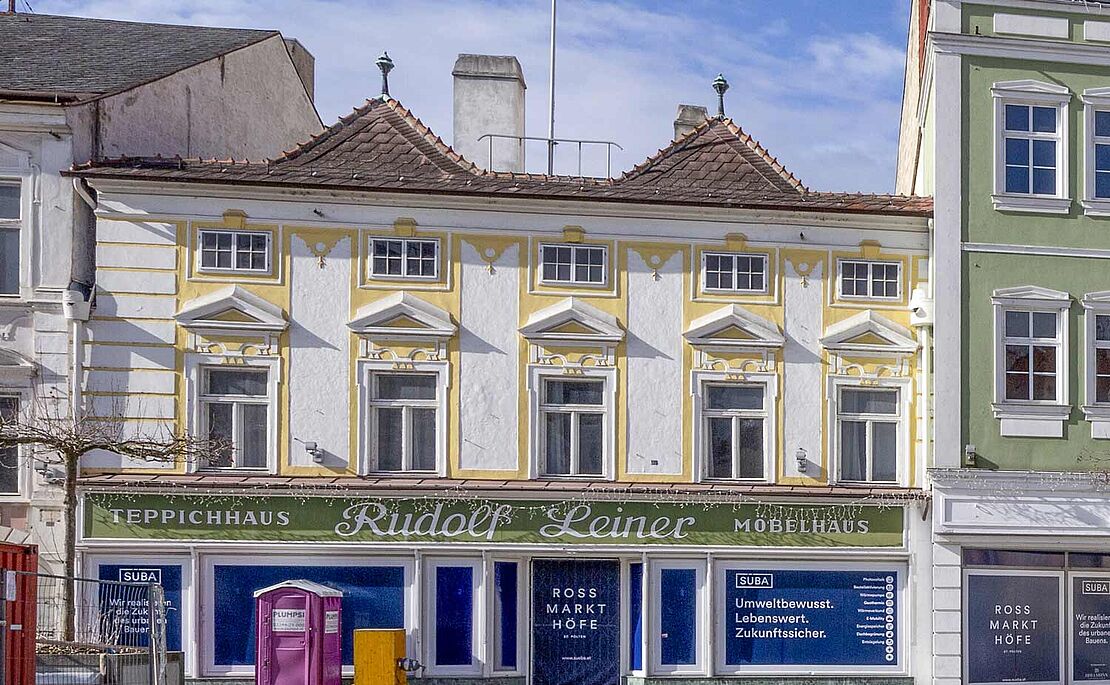 Das Stammhaus in weiß-gelb gehalten, 2-stöckig, mit grüner Firmenleiste "Teppichhaus Rudolf Leiner Möbelhaus"