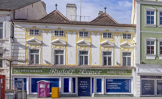 Das Stammhaus in weiß-gelb gehalten, 2-stöckig, mit grüner Firmenleiste "Teppichhaus Rudolf Leiner Möbelhaus"