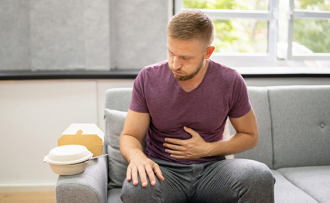 Mann auf Sofa mit einer Hand am Bauch, Völlegefühl, Blähungen