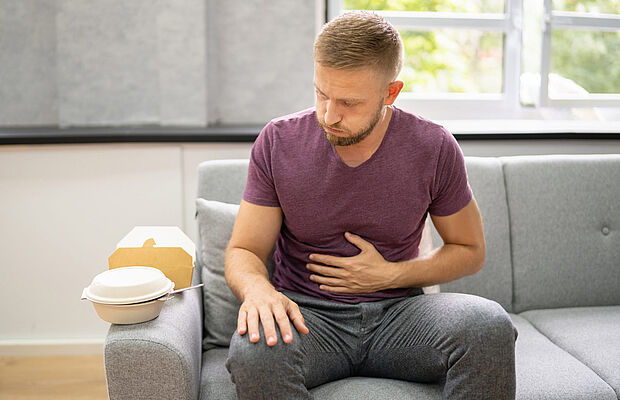 Mann auf Sofa mit einer Hand am Bauch, Völlegefühl, Blähungen