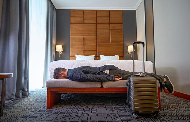 Mann liegt erschöpft auf Bett in Hotelzimmer