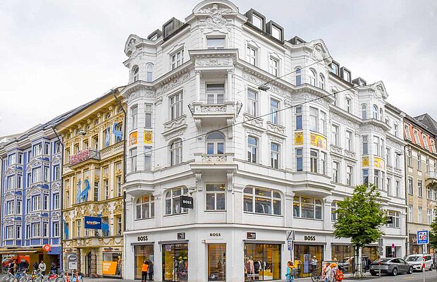 Weißes Eckhaus, links anschließend ein gelbes und blaues Zinshaus