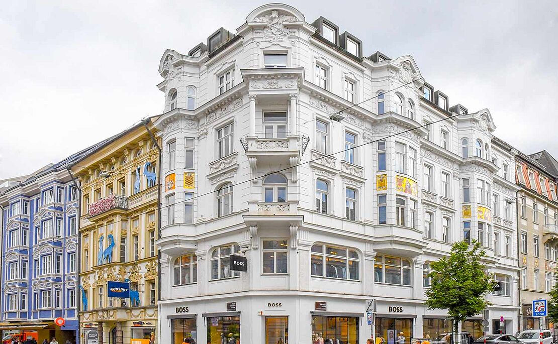 Weißes Eckhaus, links anschließend ein gelbes und blaues Zinshaus