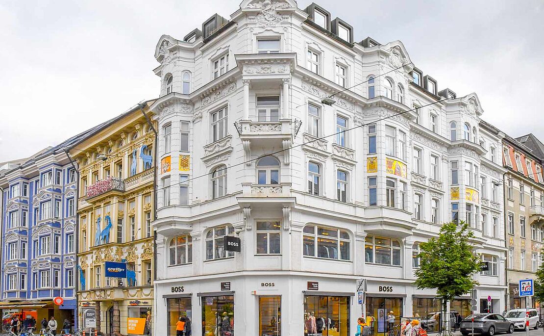 Weißes Eckhaus, links anschließend ein gelbes und blaues Zinshaus