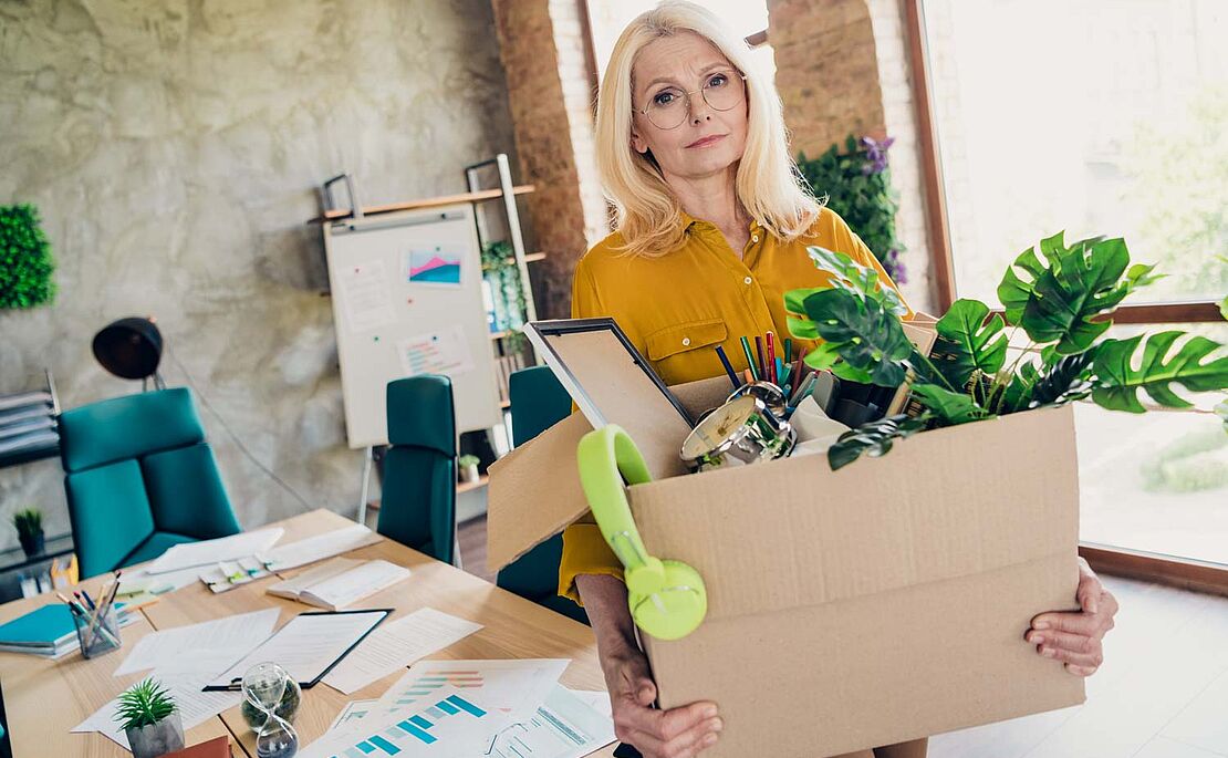 Frau mit gepackter Kiste verlässt ihr Büro