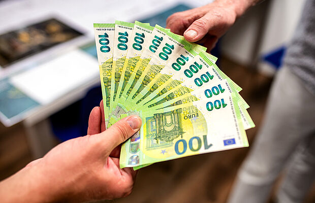 Eine Hand mit einem Fächer von 100 Euro Scheinen, zweite Hand greift zu den Scheinen