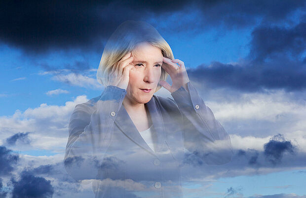 Frau, die sich aufgrund von Wetterfühligkeit mit beiden Händen an die Stirn greift