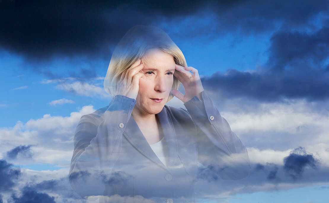 Frau, die sich aufgrund von Wetterfühligkeit mit beiden Händen an die Stirn greift