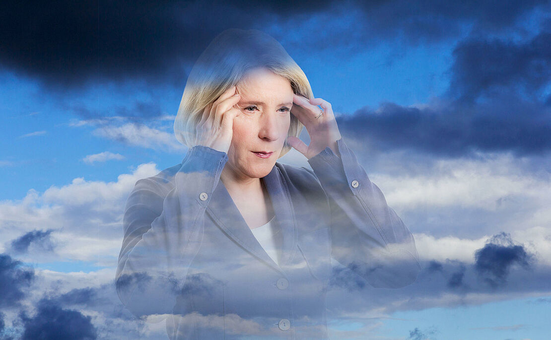 Frau, die sich aufgrund von Wetterfühligkeit mit beiden Händen an die Stirn greift