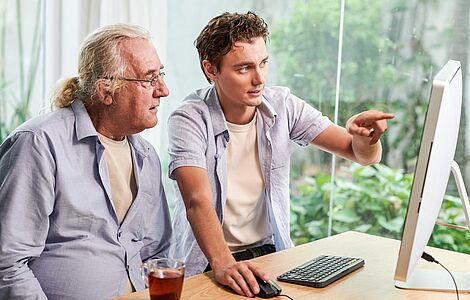 Junger Mann erklärt älterem Mann etwas auf dem Computer