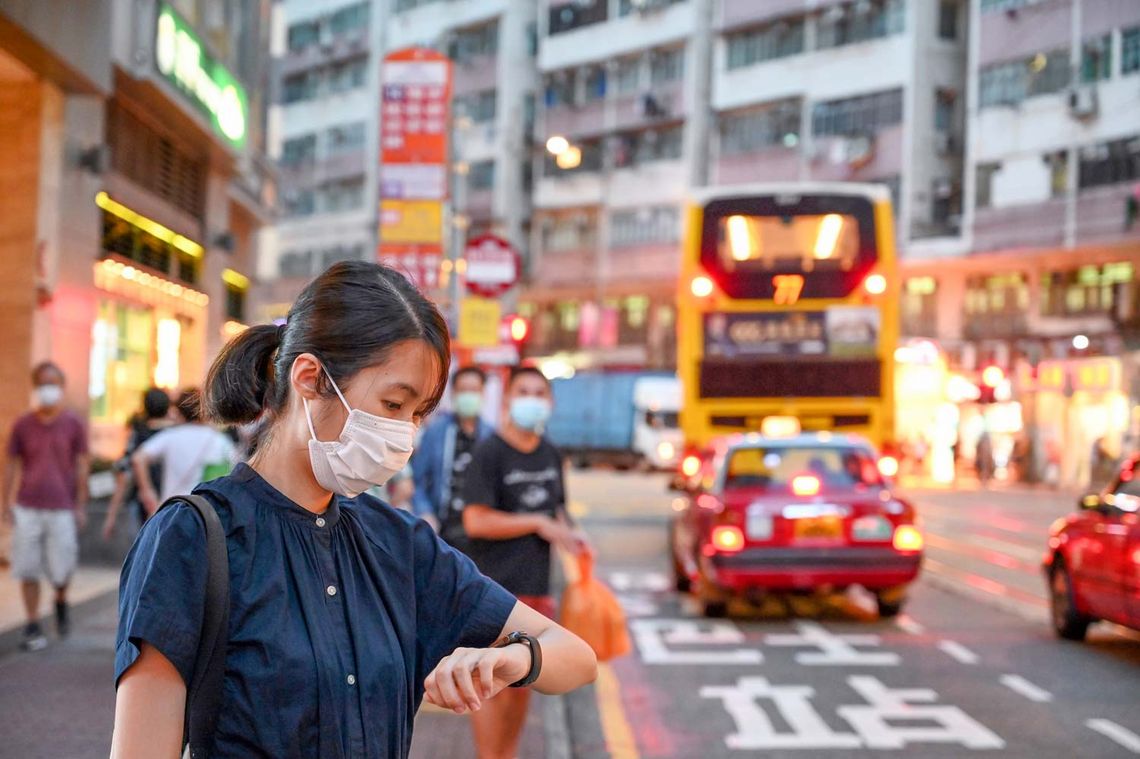 Frau in Chinas Straßen, trägt eine Maske und schaut auf die Uhr
