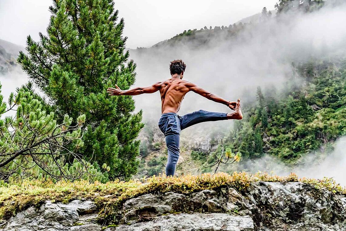 Mann mit muskulösem nackten Oberkörper praktiziert Yoga am Berg