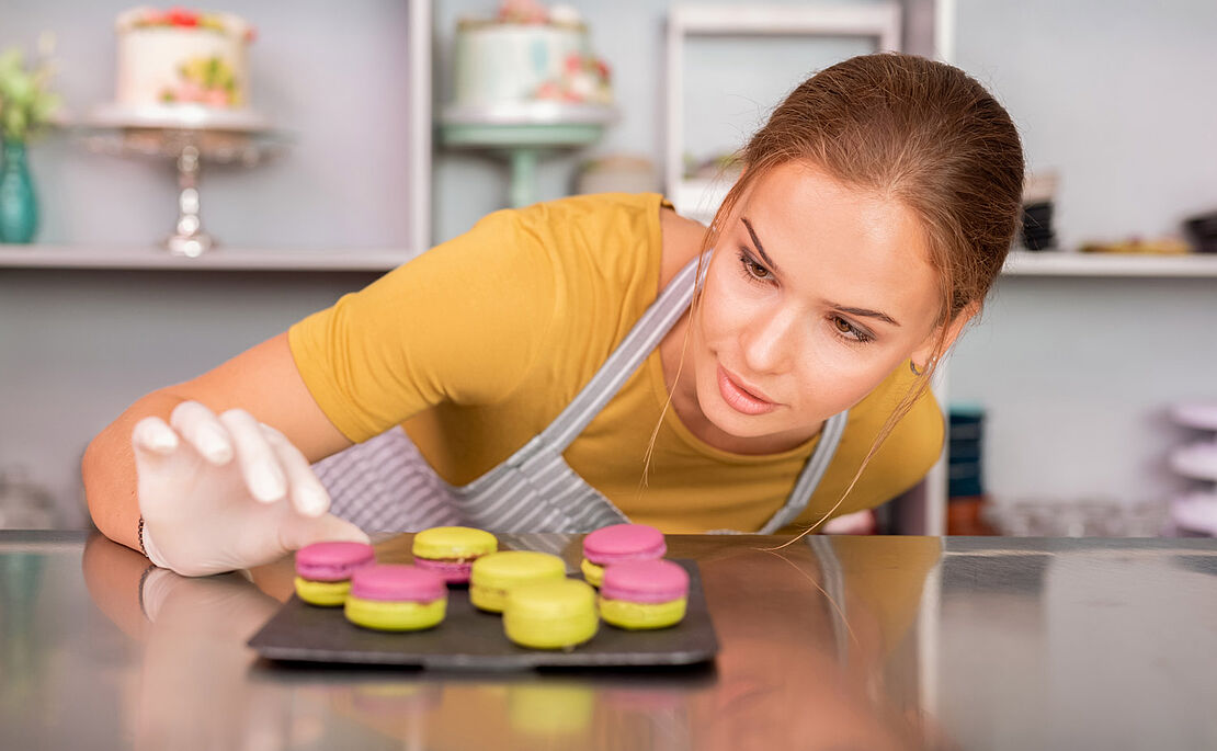 Frau mit Kochschürze, die sich über bunte Macarons beugt