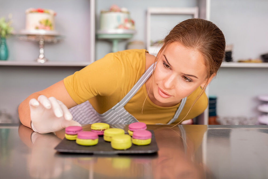 Frau mit Kochschürze, die sich über bunte Macarons beugt