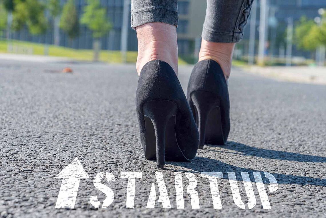 Foto von Füßen mit Stöckelschuhe die der Aufschrift und dem Pfeil "START UP" nachgehen.