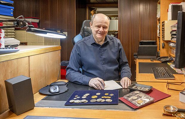Manfred Strotzka in einem Büro vor einer Münzsammlung