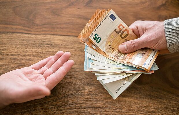 Eine offene Handfläche und eine zweite Hand, die Geldscheine zur ersten hält