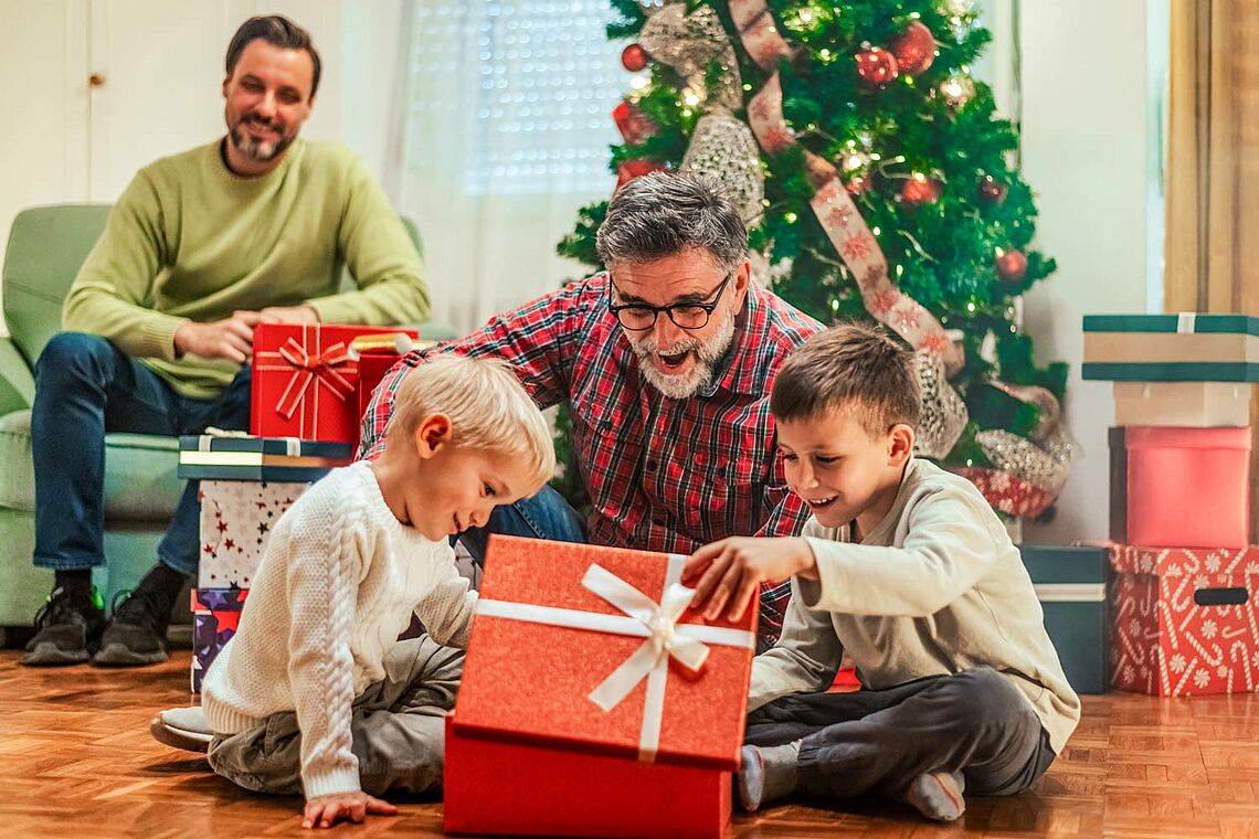 Zwei Männer mit Kinder beim Geschenke auspacken