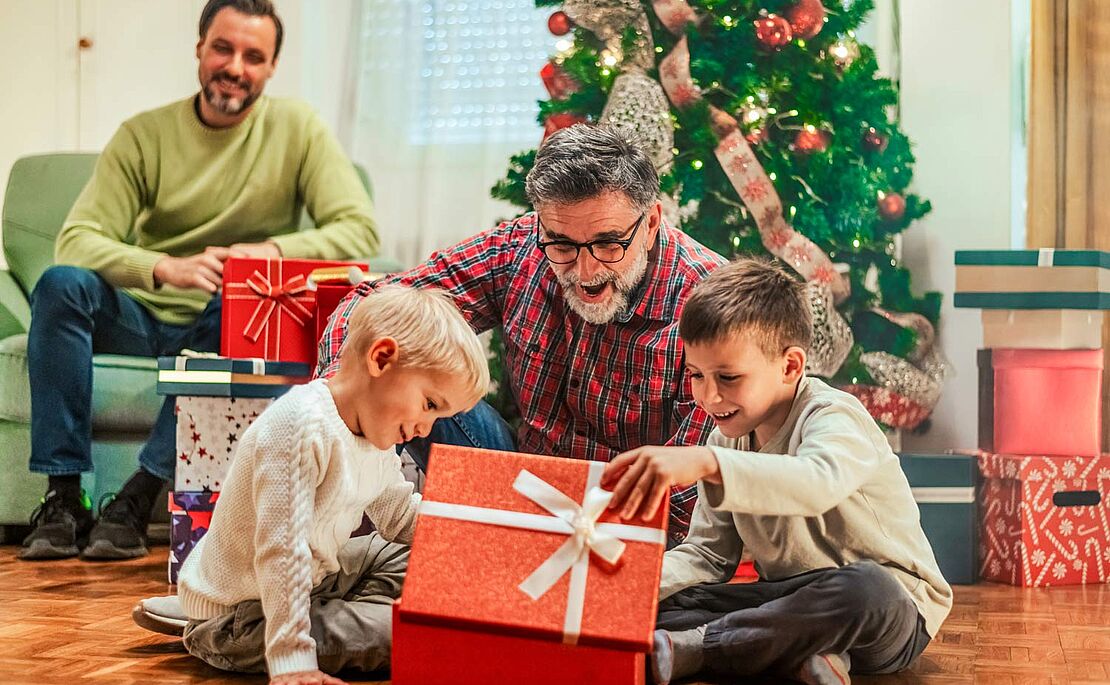 Zwei Männer mit Kinder beim Geschenke auspacken