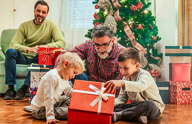 Zwei Männer mit Kinder beim Geschenke auspacken