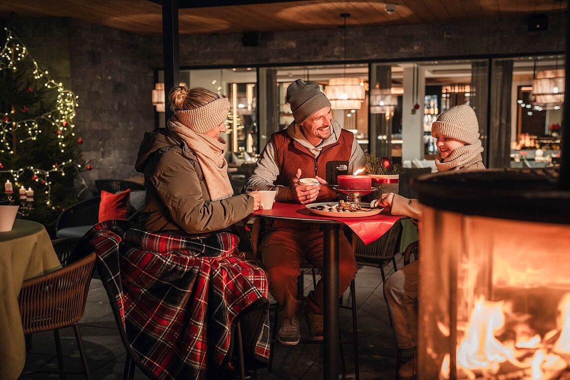 Mann, Frau, Kind vor Feuerkorb und mit Glühwein bzw. Kinderpunsch