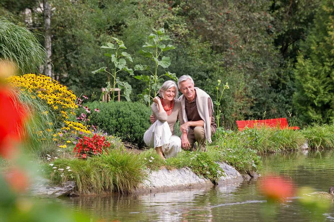 Älteres Paar sitzend an einem Teich umringt von Blumen