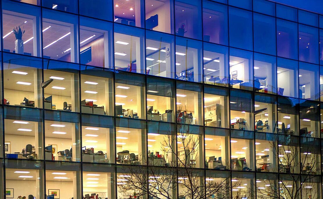 Bürogebäude mit vielen hell erleuchteten Fenstern und Mitarbeitern, die noch spät arbeiten