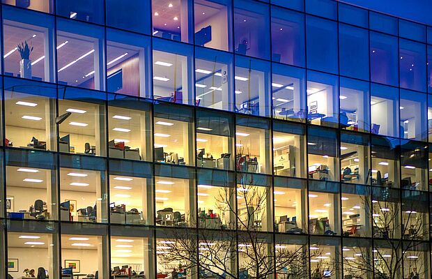 Bürogebäude mit vielen hell erleuchteten Fenstern und Mitarbeitern, die noch spät arbeiten