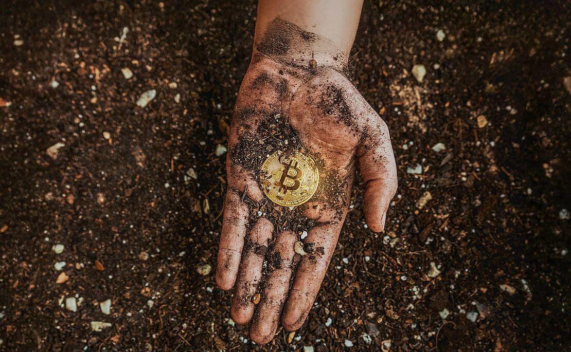 Hand über Erde, Handfläche schmutzig davon, mitten drin eine Bitcoin-Münze