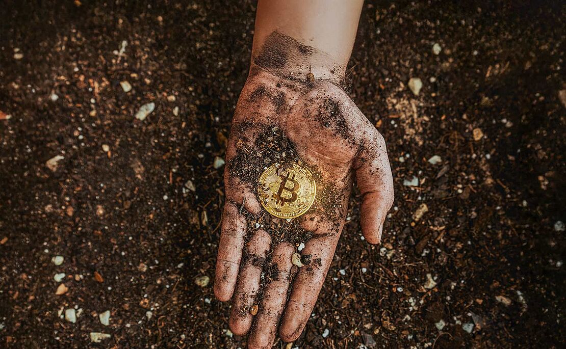 Hand über Erde, Handfläche schmutzig davon, mitten drin eine Bitcoin-Münze