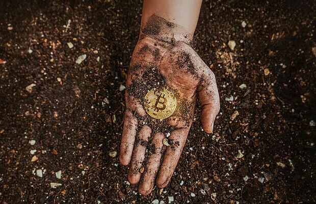 Hand über Erde, Handfläche schmutzig davon, mitten drin eine Bitcoin-Münze