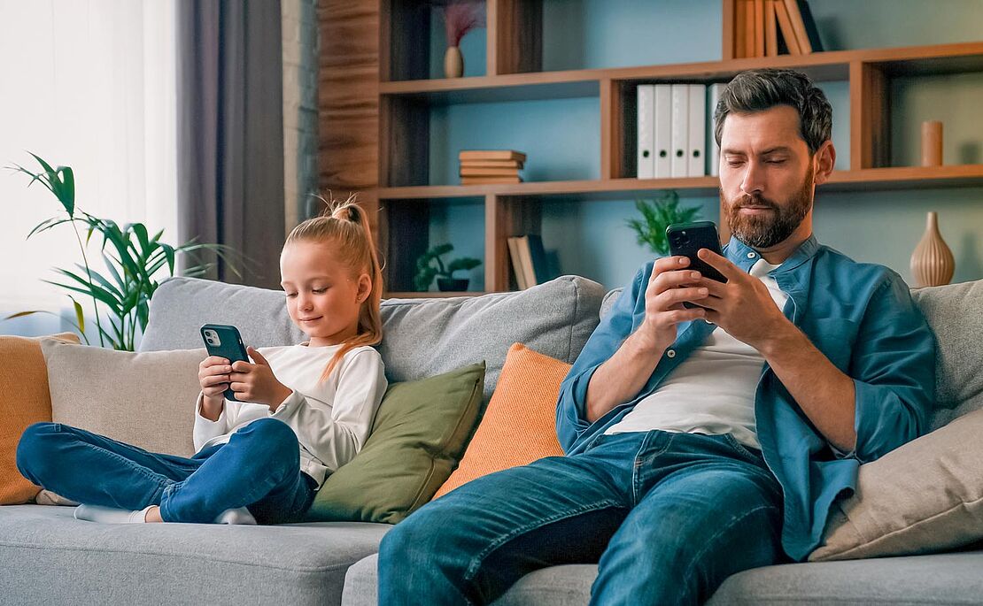 Vater und Tochter sitzen am Sofa mit Smartphone in der Hand