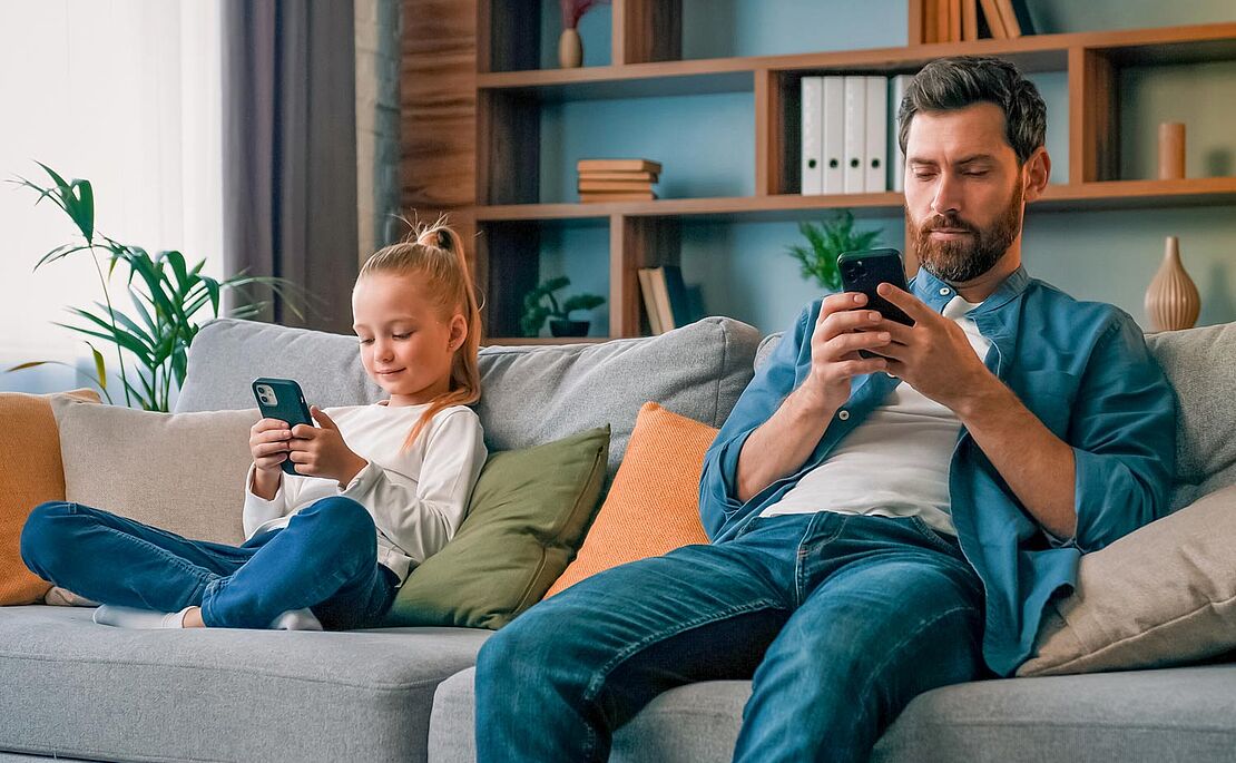 Vater und Tochter sitzen am Sofa mit Smartphone in der Hand